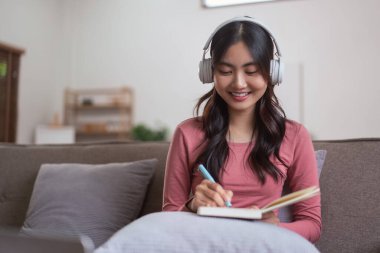 Müzik dinlerken kulaklık takan ve evdeki yaşam tarzıyla günlük defterine notlar yazan kadınlar..