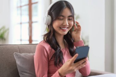 Akıllı telefondan müzik dinlemek için kulaklık takan kadınlar evdeki yaşam tarzında kanepede dinlenirken....