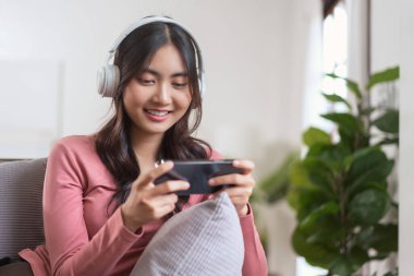 Kulaklık takan kadınlar akıllı telefonlarıyla video oyunu oynarken evdeki yaşam tarzlarıyla kanepede boş vakitler geçiriyorlar..