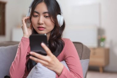 Kulaklıklı kadınlar akıllı telefonlarıyla video konuşmalarında boş vakitlerinde evdeki yaşam tarzlarında kanepede oturuyorlar..