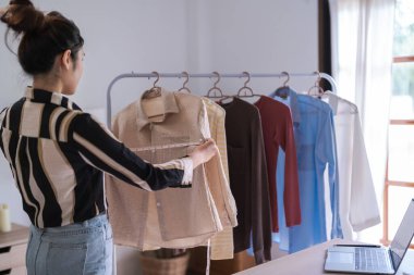 Moda tasarımcısı kadınlar elbise askılığındaki elbise kolleksiyonunun boyunu ölçmek için mezura kullanırlar..