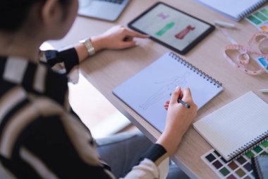 Moda tasarımcısı kadınlar tablette ayrıntılara bakıyor ve yaratıcı yeni koleksiyon için kıyafet çiziyorlar.