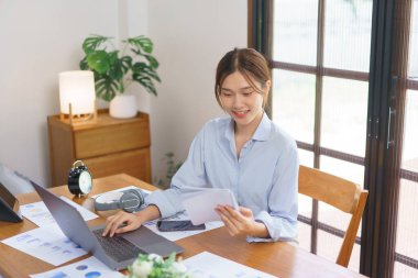 Business at home concept, Businesswoman is reading marketing data in notebook and working on laptop.