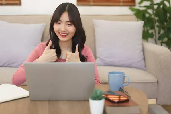 Young businesswoman showing thumbs up gesture and talking with partners while meeting in video call.