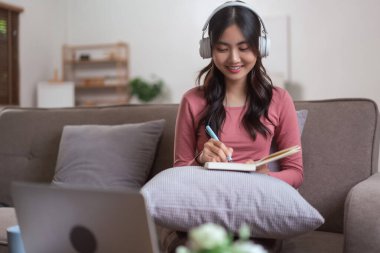 Kadınlar internetten eğitim alırken kulaklık takar ve evdeki yaşam tarzında not defterine not alır..