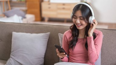 Kulaklıklı kadınlar akıllı telefonlarıyla video konuşmalarında boş vakitlerinde evdeki yaşam tarzlarında kanepede oturuyorlar..