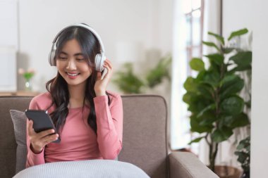 Kulaklıklı kadınlar akıllı telefonlarıyla video konuşmalarında boş vakitlerinde evdeki yaşam tarzlarında kanepede oturuyorlar..