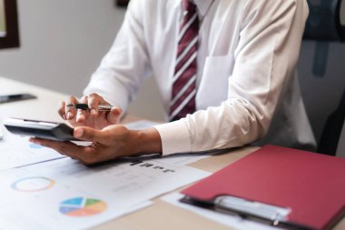 İş adamı, projenin maliyetini hesaplamak ve başlangıcın pazarlama belgesini kontrol etmek için hesap makinesi kullanır.