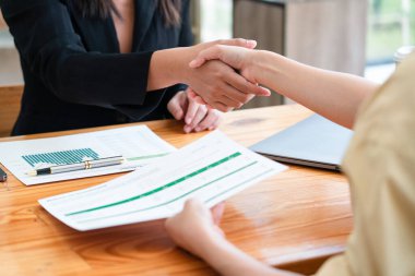 İki iş kadını yeni iş anlaşmasıyla kağıt okuduktan sonra el sıkışıyor..