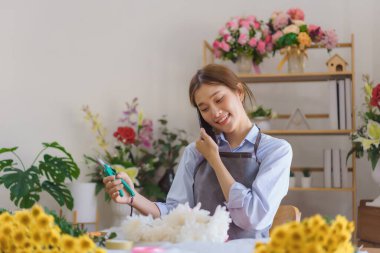 Çiçekçi konsepti, elinde budama makası tutan ve çiçekçide akıllı telefondan konuşan kadın..