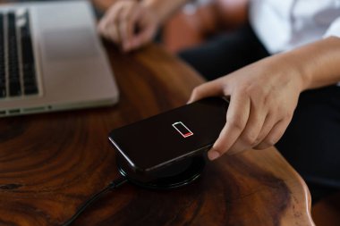 İş adamının elleri cep telefonunu şarj etmek için akıllı telefonu kablosuz şarj cihazına bağlıyor..