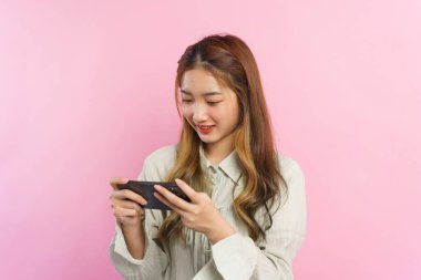 Pembe arka planda izole edilmiş akıllı telefondan gülümseyen ve oyun oynayan genç kadınlar.