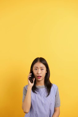 Genç kadınlar iletişim kuruyor ve sarı arka planda izole edilmiş akıllı telefondan konuşuyorlar..