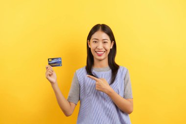 Young women smiling and showing credit card for online shopping isolated on yellow background.