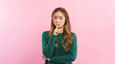 Young women using forefinger on mouth to making silent gesture isolated on pink background.