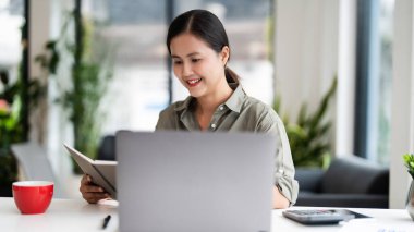 Asian casual businesswoman reading business data on book and working about finance report on laptop.