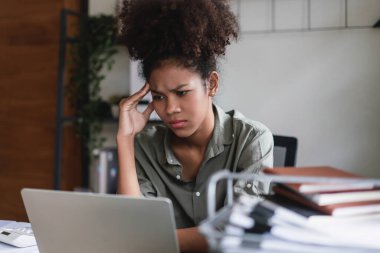 Afrikalı Amerikalı iş kadını baş ağrısı ve stresli dizüstü bilgisayardaki finans verilerini okurken.
