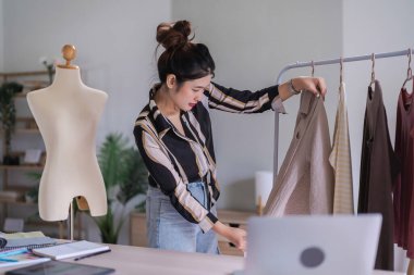 Fashion designer women using measure tape to measuring size of new collection dress on clothes rack.