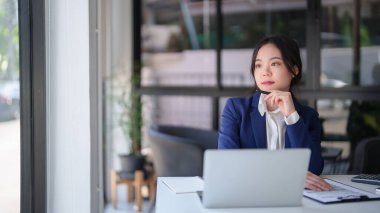 İş kadınları pencerenin dışına bakıyor ve finans belgesini okurken ve iş yerinde dijital dizüstü bilgisayar üzerinde çalışırken yeni başlatılan proje hakkında strateji yatırımları ve yönetimi analiz etmeye özen gösteriyorlar..