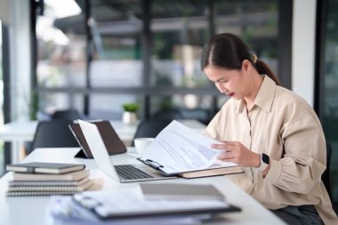 Orta yaşlı iş kadını teknoloji dizüstü bilgisayarında piyasa ticaret verileri okuyor ve modern işyerindeki yatırım ve yeni girişimlerin stratejisini analiz etmeyi düşünürken finans belgesini kontrol ediyor.