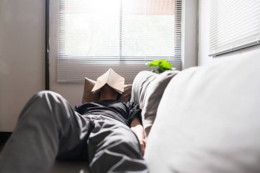 Akıl sağlığı sorunu olan bir adam rahat koltukta uzanıyor ve yüzünü kitapla örtüyor..