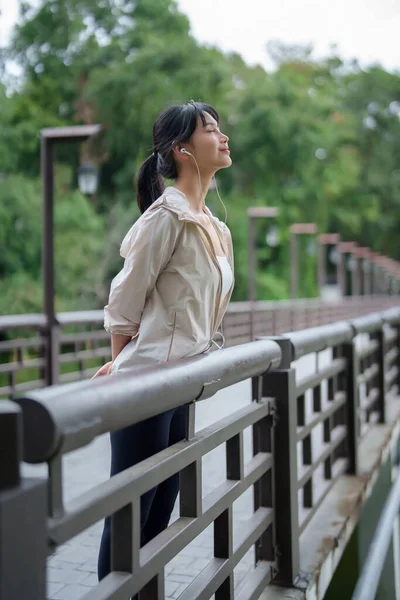 Genç Asyalı koşucu kadınlar gölün yanında durup kulaklık takarak parkta antrenman yaptıktan sonra dinlenmek ve sağlıklı yaşam tarzı için spor yapmak için kulaklık takıyorlar..