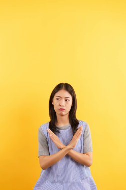 Dur işareti yapan genç kadınlar çapraz eller ve izole edilmiş sarı arka planda öfkeli bir yüz..