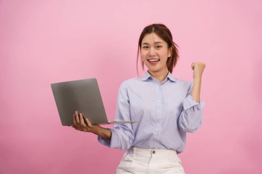 Dizüstü bilgisayar tutan ve yumruğunu sıkan kadınlar pembe arka planda izole edilmiş kutlama jestleri yapıyorlar..