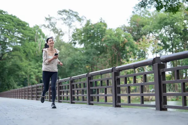 Young asian runner women wearing earphones to listening the music on smartphone and running in the park while workout and fitness exercise for healthy wellness lifestyle in morning at outdoor jogging.