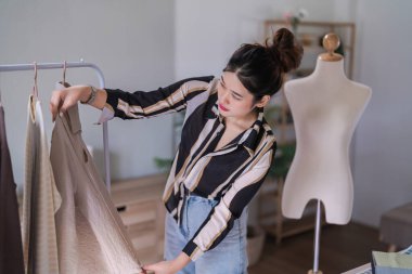 Fashion designer women using measure tape to measuring size of new collection dress on clothes rack.