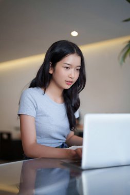 Bir kitap okuduktan sonra ödev yapmak için dizüstü bilgisayarda yazı yazan ve araştırma yapan Asyalı genç kız öğrenci kafe 'de eğitim bilgisi üzerine online dersler izledi..