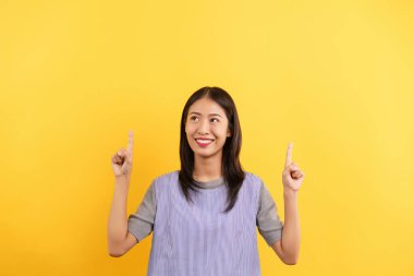 Young women pointing finger up with both hands to present something isolated on yellow background.