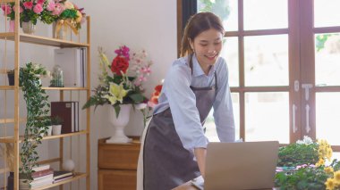 Çiçekçi konsepti, çiçekçi kadın çiçekçi çiçekçide çalışırken dizüstü bilgisayardan müşteri siparişini kontrol ediyor..