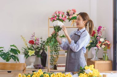 Floristry concept, Woman florist holding white chrysanthemum with smiling happiness in flower shop.