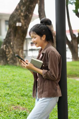 Bir lise öğrencisi okul binasının önünde telefonuna bakarak yürüyor. Gülümsüyor ve telefonuyla meşgul görünüyor..