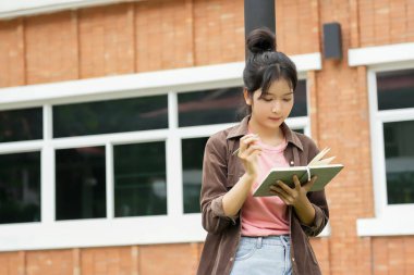 Bir lise öğrencisi okul binasının önünde telefonuna bakarak yürüyor. Gülümsüyor ve telefonuyla meşgul görünüyor.