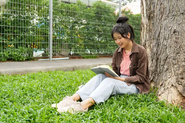 Modern bir okul binasının önünde oturan bir lise öğrencisi deftere bir şeyler yazıyor. Kahverengi ceket ve açık mavi kot giyiyor. Yazılarına odaklanmış.. 