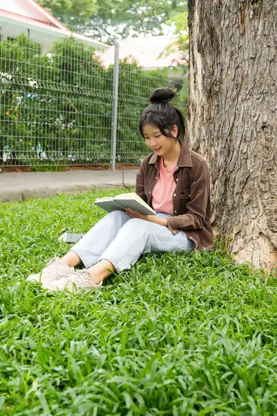 Modern bir okul binasının önünde oturan bir lise öğrencisi deftere bir şeyler yazıyor. Kahverengi ceket ve açık mavi kot giyiyor. Yazılarına odaklanmış.. 