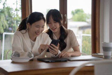 İki iş kadını, yeni projenin yatırımları ve iş arkadaşlığı konuşmalarının iş yerinde başarılı olması üzerine birlikte çalıştıktan sonra akıllı telefonu kullanarak birlikte sörf yapıyor..