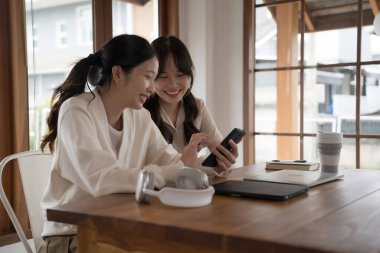 İki iş kadını, yeni projenin yatırımları ve iş arkadaşlığı konuşmalarının iş yerinde başarılı olması üzerine birlikte çalıştıktan sonra akıllı telefonu kullanarak birlikte sörf yapıyor..