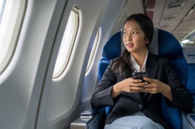 İş kadını akıllı telefondan finans sektörü raporlarını okurken aynı zamanda tatil yaşam tarzı sırasında uçakla seyahat sınıfı uçuşuna pencerelerin yanında oturup mesaj yazarak sohbet ediyor..