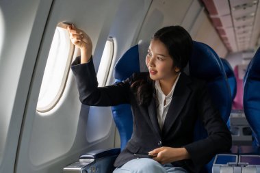 İş kadını akıllı telefon kullanarak finans sektörü raporlarını okuyor. Pencerelerin yanında oturmuş, tatildeyken uçakla iş seyahati sınıfı uçuşunu izliyor..