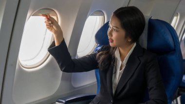 İş kadını akıllı telefon kullanarak finans sektörü raporlarını okuyor. Pencerelerin yanında oturmuş, tatildeyken uçakla iş seyahati sınıfı uçuşunu izliyor..