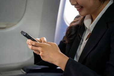 İş kadınının akıllı telefondan mesajlar yazıp finansal iş raporlarını okurken tatilde uçakta uçuş işi seyahatinin pencerelerinin yanında oturması..