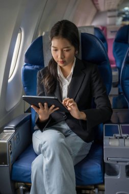 İş kadınları yeni başlayan projenin kar ve finansmanı hakkındaki iş raporlarını kontrol etmek için tablet kullanarak ve okuyarak uçak seyahatleri sırasında pencere kenarında otururken,.