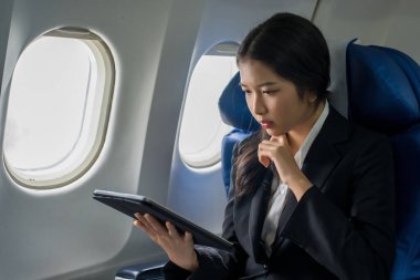 İş kadınları, uçak seyahatleri sırasında pencere kenarında otururken strateji analizi için tablet üzerine yeni başlatılan kâr ve finans projeleri hakkında iş raporlarını kontrol etmek için okurken,.