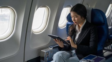 İş kadınları yeni başlayan projenin kar ve finansmanı hakkındaki iş raporlarını kontrol etmek için tablet kullanarak ve okuyarak uçak seyahatleri sırasında pencere kenarında otururken,.