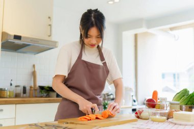 Asyalı kadınlar, kahvaltı hazırlamak için taze sebzeler hazırlarken evdeki mutfakta sağlıklı yiyecek yaşam tarzını hazırlamak için tahtanın üzerinde bıçakla havuç doğruyor..