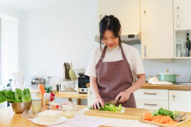 Asyalı kadınlar, kahvaltı hazırlamak için taze sebze hazırlarken evdeki mutfakta sağlıklı yiyecek yaşam tarzını hazırlarken tahtanın üzerinde bıçakla marul doğruyor..