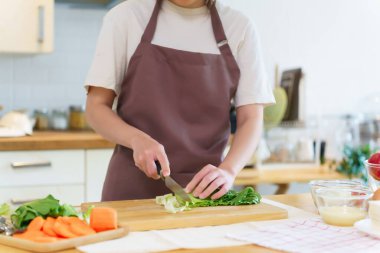 Asyalı kadınlar, kahvaltı hazırlamak için taze sebze hazırlarken evdeki mutfakta sağlıklı yiyecek yaşam tarzını hazırlarken tahtanın üzerinde bıçakla marul doğruyor..